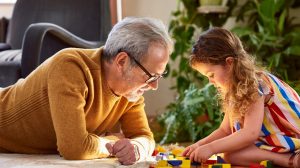 Granddaughter playing with wooden block and granddad watching