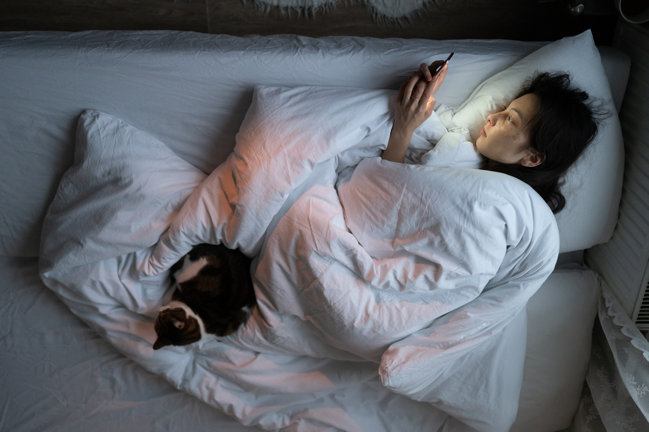 Una mujer con depresión tumbada en la cama y consultando el móvil.
