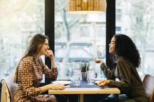 Dos chicas mirándose y comiendo en un restaurante.