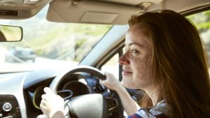 Smiling young woman with freckles driving car looking sideways