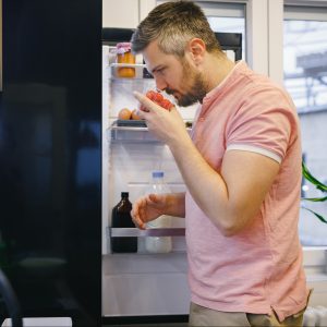 Man standing in the kitchen, holding a box of cherry tomatoes and smelling it