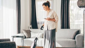 Woman doing house work. Woman talking on cell phone while vacuuming floor.