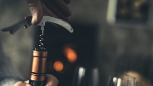 Close-up of a man, with a corkscrew in his hand, opening a bottle of white wine.