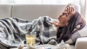 Woman having symptoms of Covid-19 lies covered in blanket in isolation with handerchiefs and pills next to her.