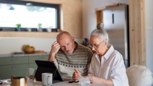 Senior couple sitting at the kitchen table looking at digital tablet and recalculating their expenses.