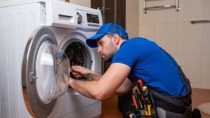 Working man plumber repairs a washing machine in home. Washing machine installation or repair. plumber connecting appliance