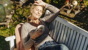 Woman with cup of coffee relaxing on garden bench