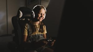 Smiling girl playing video game at home in dark