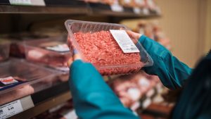 Una persona comprando una bandeja de carne picada en el supermercado.