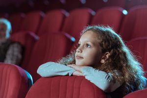 Una niña en edad adolescente observa atentamente la pantalla en una sala de cine.