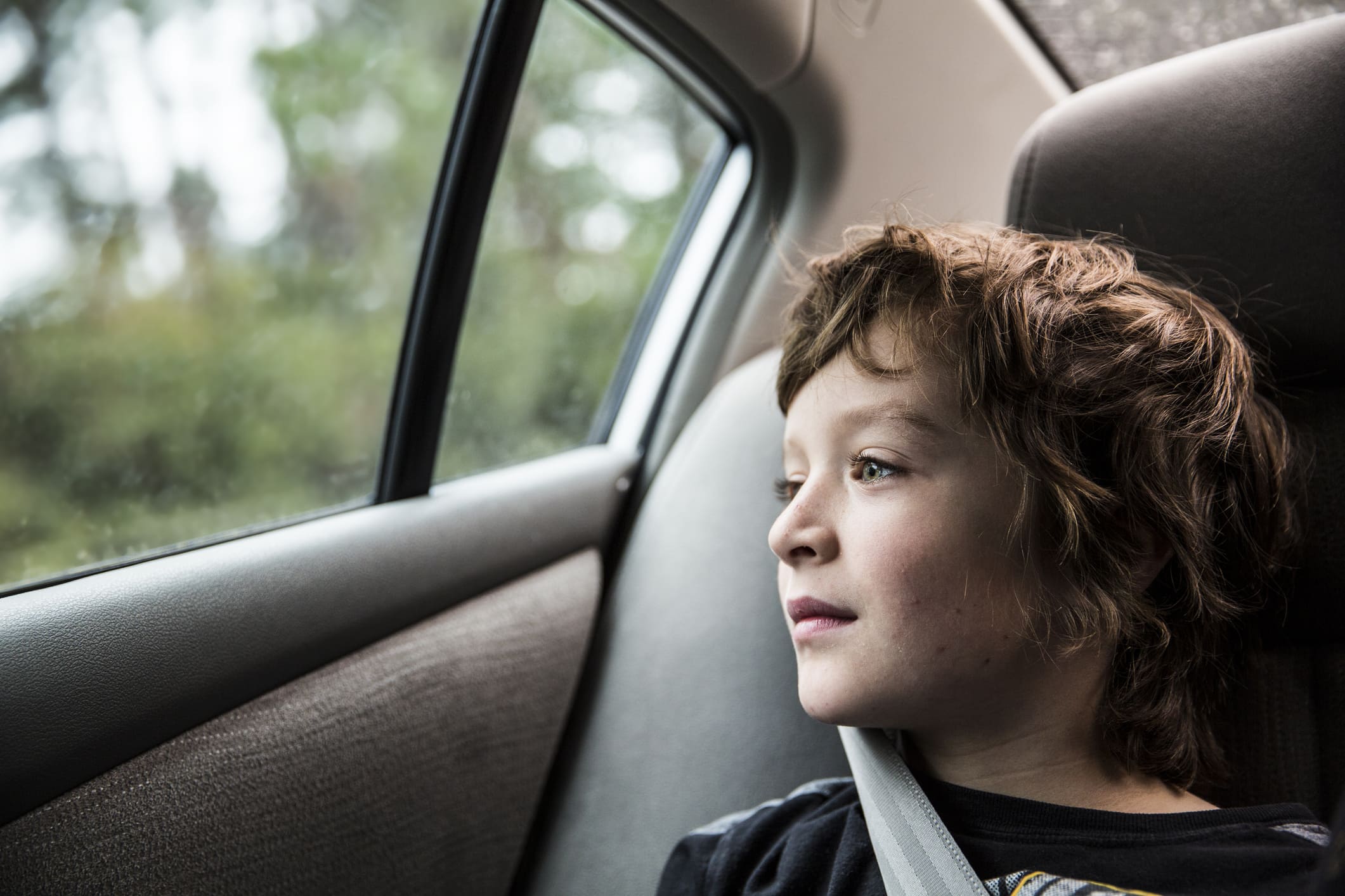 Niño mirando desde la ventana del coche con el cinturón de seguridad puesto.