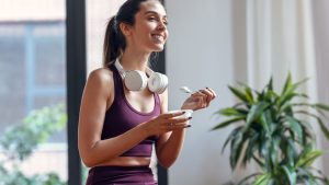Sporty young woman eating a yogurt while sitting on fitness ball at home.