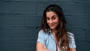 Woman in urban clothes and long hair in front of a brick wall with the arms crossed and a funny expression
