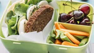 Healthy school food in a lunch box, vegetarian sandwich with cheese, lettuce, cucumber, egg and cress, sliced carrot and celery, cherries and pear