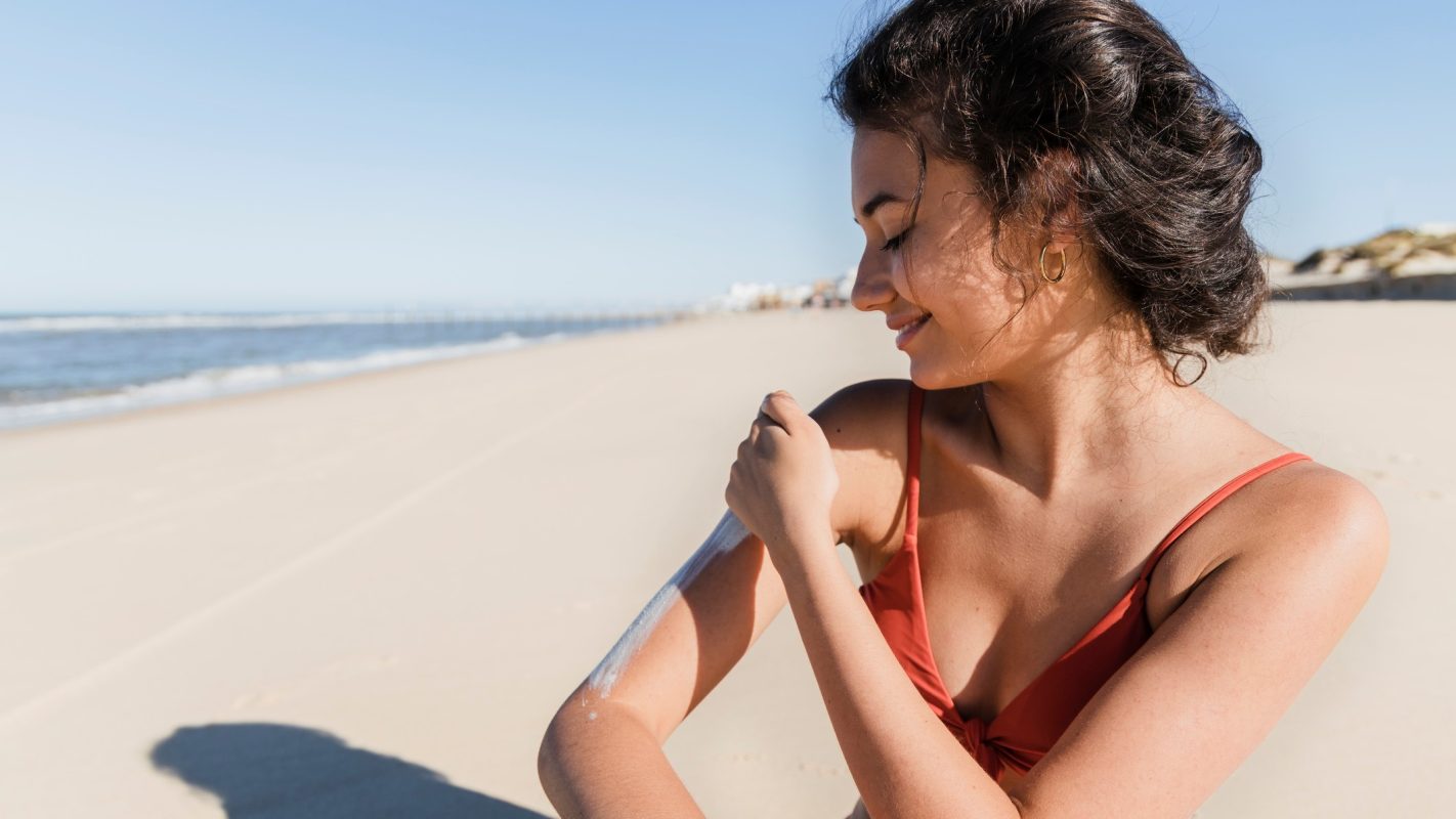 Una chica poniéndo crema solar en la playa.