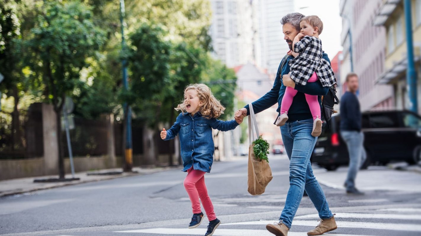 Un padre sujetando a sus dos hijas por la calle.