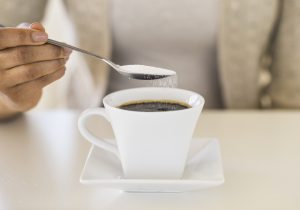 Una persona endulzando su café con azúcar.
