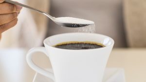 Una persona endulzando su café con azúcar.