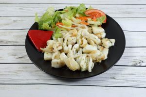 Portion of grilled cuttlefish garnished with lettuce and red pepper, on wooden table
