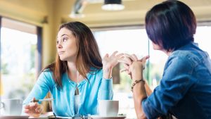 Annoyed teen girl talking to mother in coffee shop
