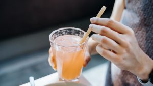 Close up shot of young woman drinking a glass of fresh iced pink lemonade with eco-friendly straws during meal in cafe. Sustainable lifestyle, eco trend, going green lifestyle