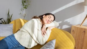 Young beautiful woman enjoying sunlight resting on sofa at home. Simple living concept