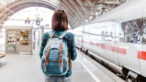 A young tourist girl with backpack waits for train on railway station