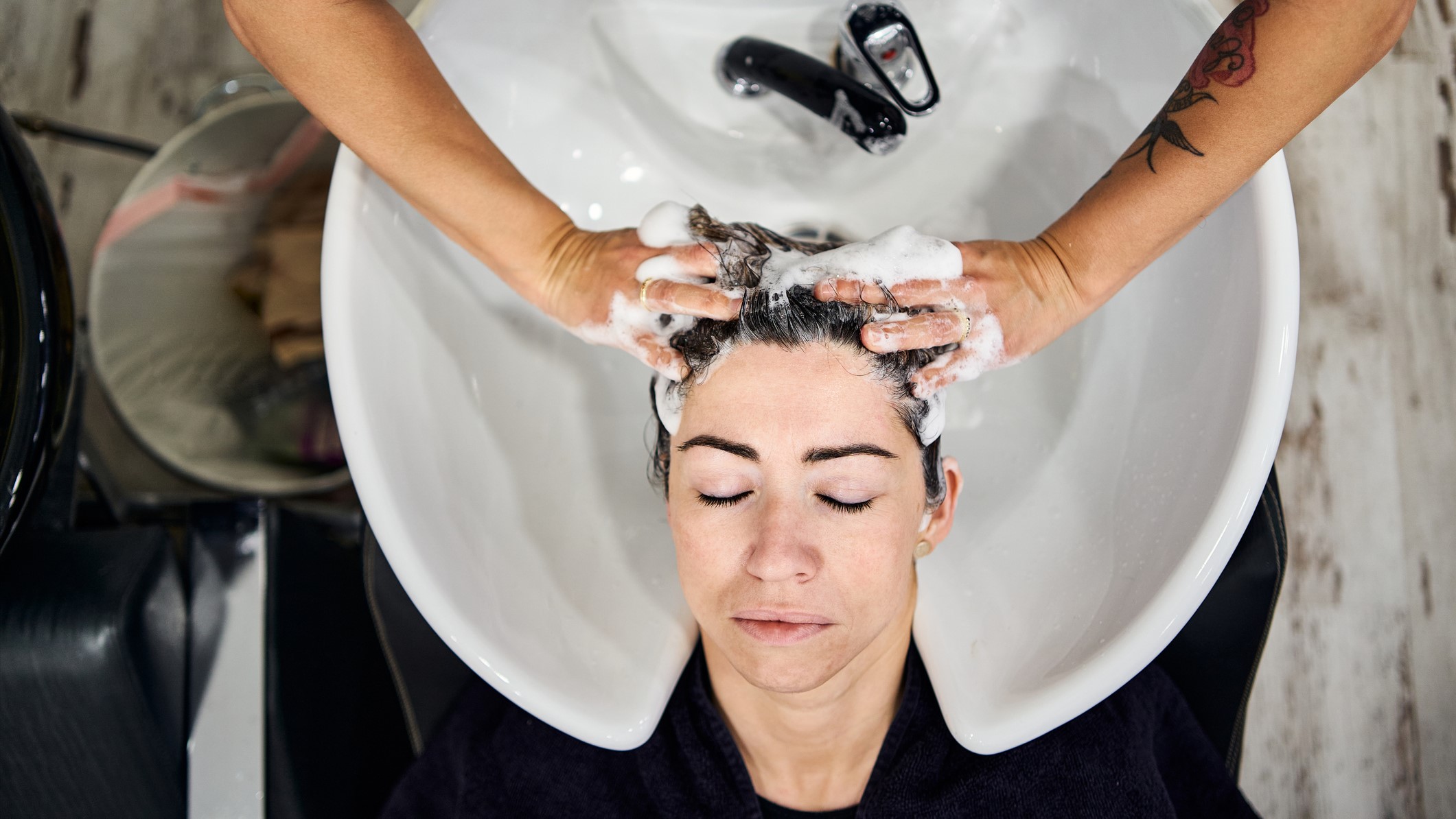 Una peluquera lava el pelo a una cliente en su peluquería.