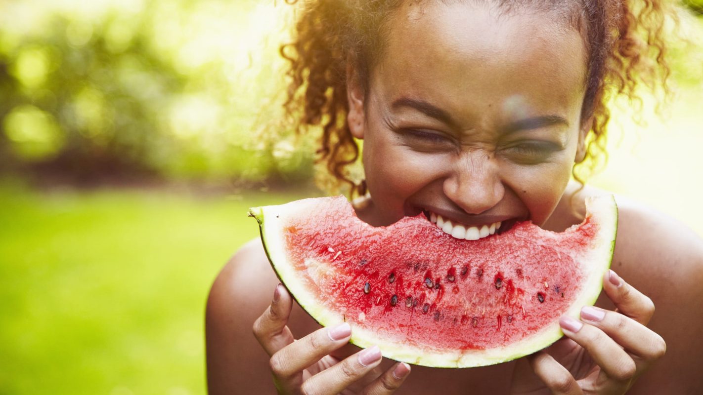 Una chica mordiendo una rodaja de sandía.