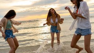 Group of Asian woman friends playing together on tropical island beach at summer sunset.