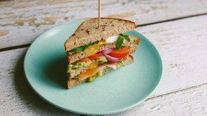 Delicious toast of dark bread with salmon, cheese, cucumber and tomato in blue plate. Healthy vegetarian food.