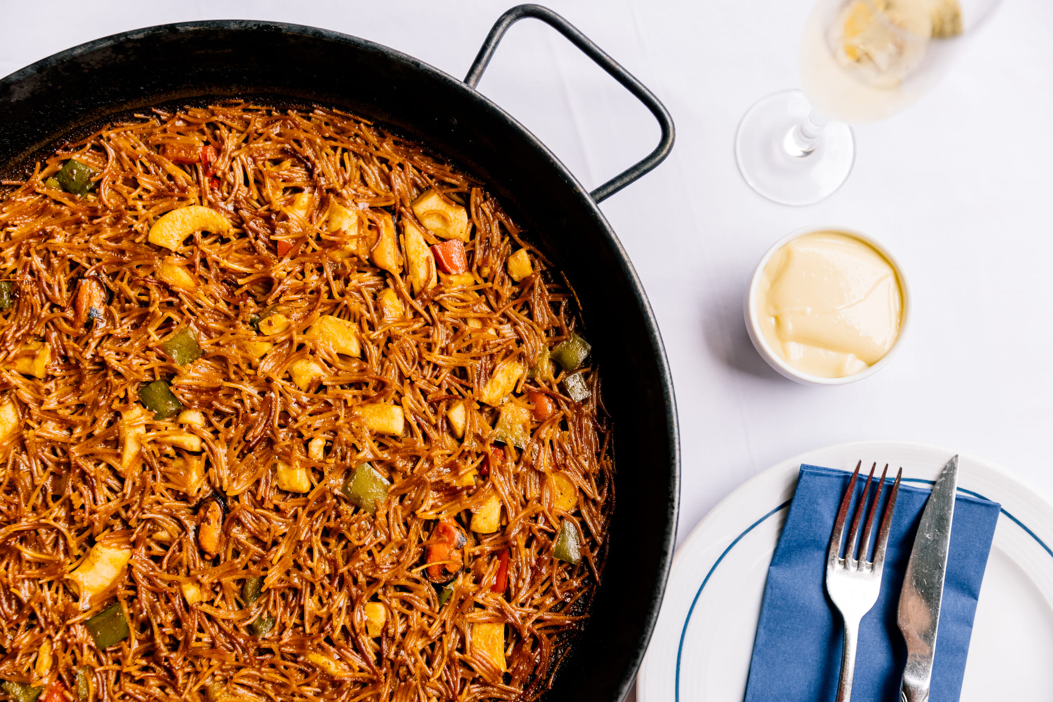 Fideuà servida en una sartén con verduras en un restaurante.