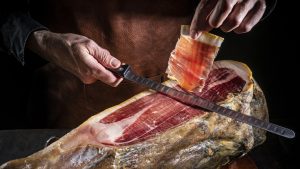 Iberian ham serrano ham cutting slice male hands and knife on dark moody