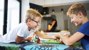 Two brothers laughing playing a board game on the kitchen table
