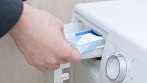 Una persona depositando polvos de la lavadora en el cajetín de esta.