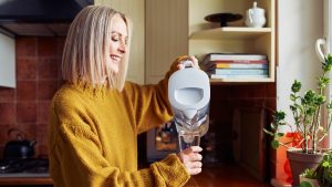 Smiling mature woman pouring filtered water into glass at kitchen