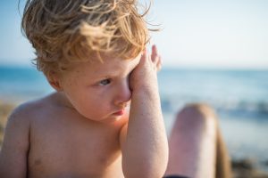 Un niño se rasca los ojos en la playa.