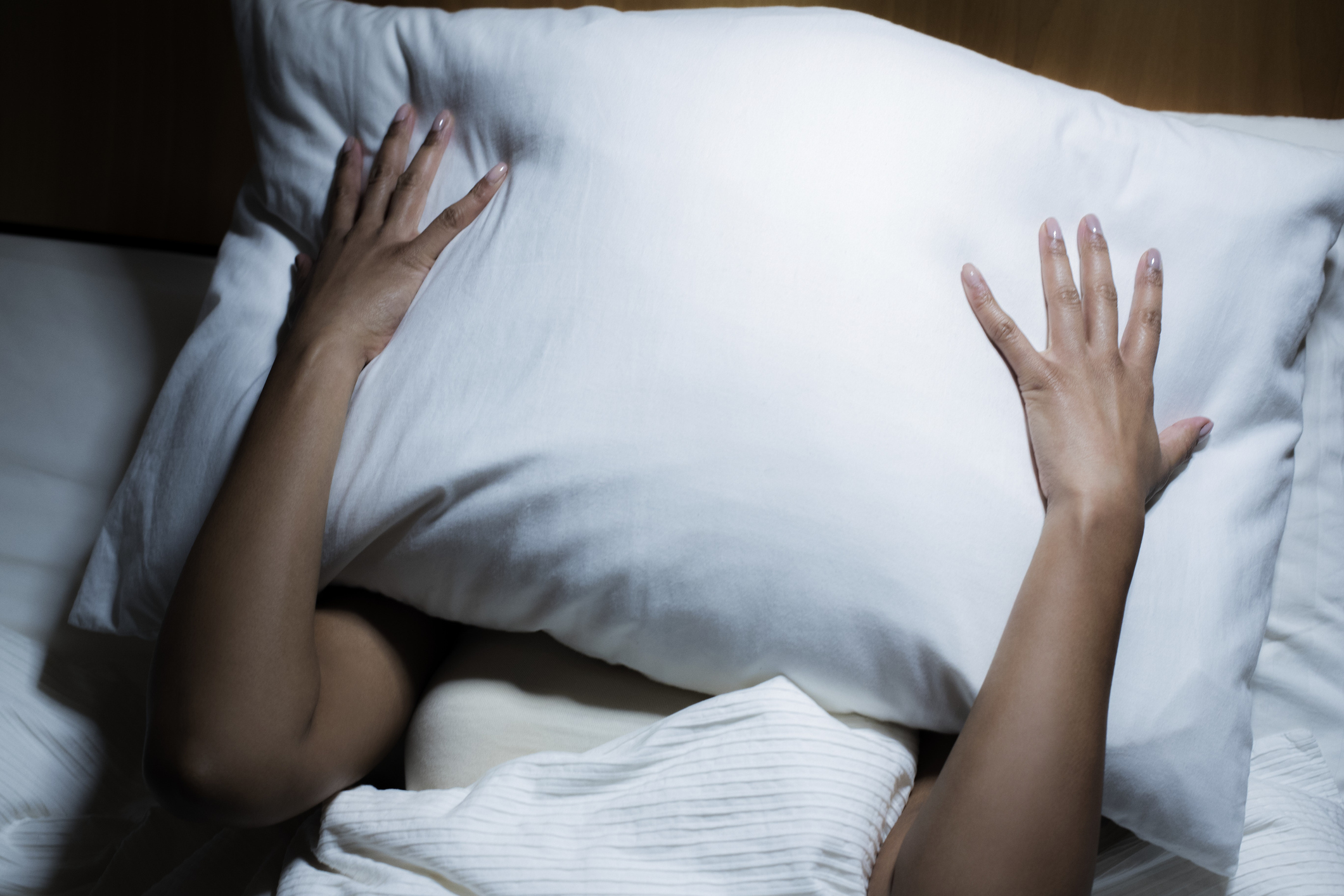 Una chica se tapa la cara con la almohada en la cama.
