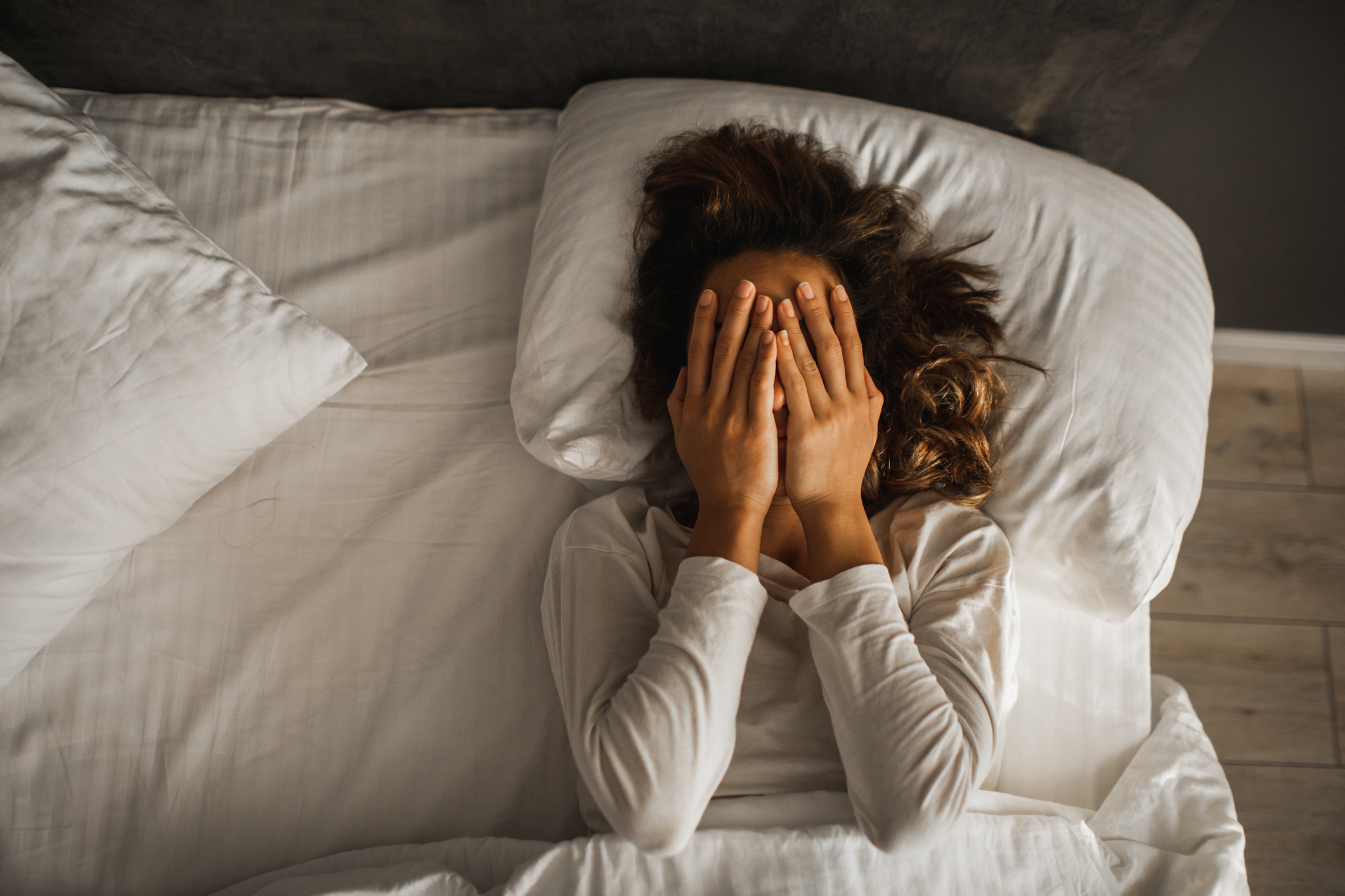 Mujer tumbada en la cama tapándose la cara tras el sueño que acaba de tener.