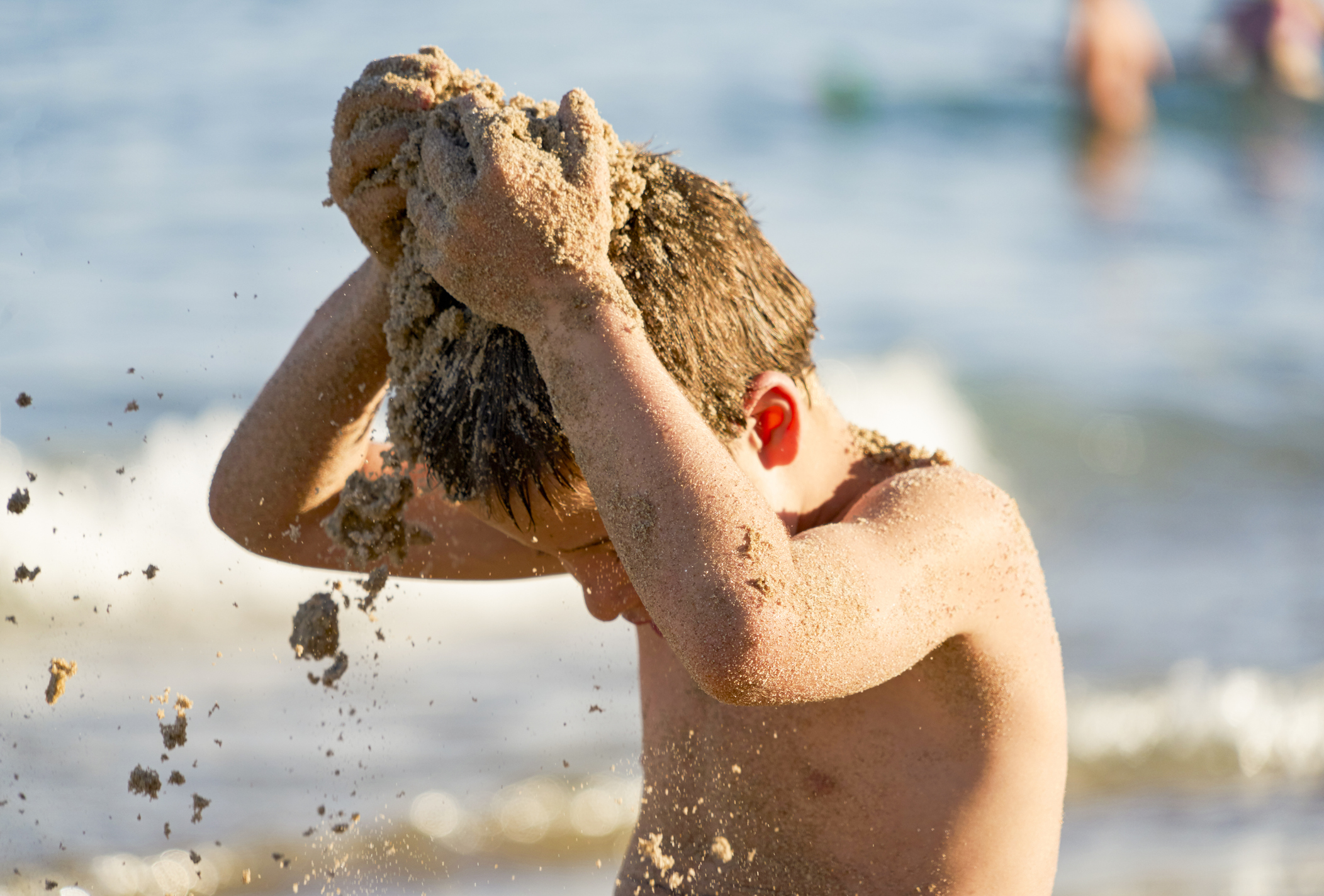 Un niño se tira arena a sí mismo en plena playa.