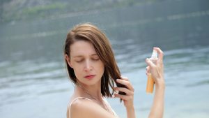 Woman applying sunscreen spray on the beach, hair care protection concept