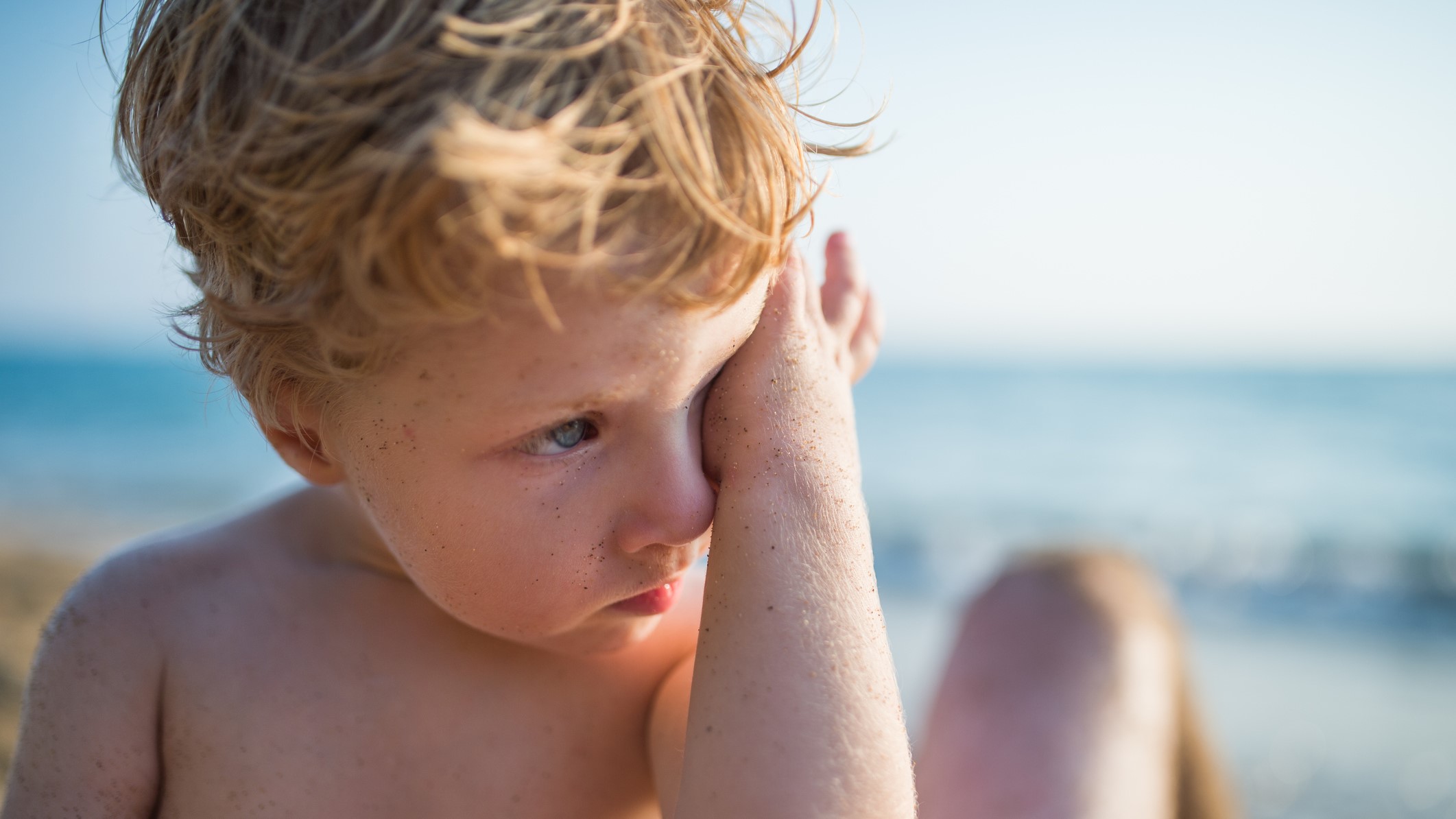 Un niño se rasca el ojo en la playa.