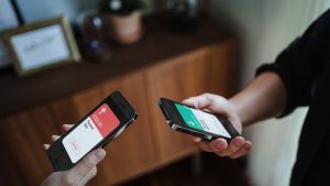 Cropped shot of a man and a woman's hand holding smartphone, sending money through digital wallet, using online banking mobile app device. Friends holding mobile phone to activate NFC. Smart banking with technology