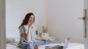 Young woman eating pizza while watching movie on laptop in bedroom at home