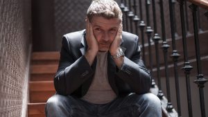 unemployment and divorce - dramatic lifestyle portrait of sad and depressed man on his 40s sitting indoors on staircase thoughtful and worried suffering depression problem