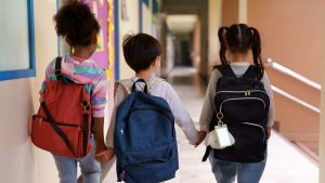 Back view of children holding hands together walking to school