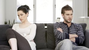 Couple sitting on sofa with arms folded, looking angry