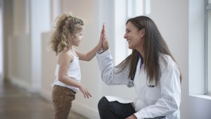 Caucasian doctor and girl high-fiving in hallway