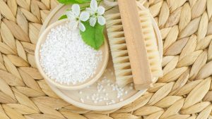 Epsom bath salt and wooden massage foot brush with natural bristles. Eco friendly toiletries set. Natural beauty treatment, pedicure, skin care or zero waste concept. Selective focus.