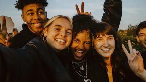 Portrait of cheerful friends taking selfie outdoors during sunset